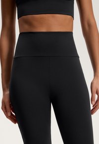 Črne hlače z visokim pasom, izdelane iz gladkega in raztegljivega materiala. Imajo brezšivno zasnovo z širokim pasom za udobje.