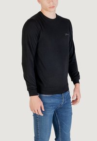 Maglione nero a maniche lunghe con collo a giro, realizzato in un materiale morbido, con un logo discreto sul petto e polsini e orlo a costine.