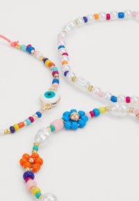 Colorful beaded necklaces featuring pearls, a gold eye charm, and flower motifs. Includes various shapes and bright accent colors.