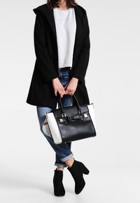 Bolso en blanco y negro con un diseño estructurado, que presenta un detalle de lazo y acentos dorados. Fabricado en cuero suave con colores en contraste.