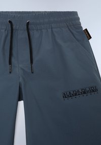 Shorts légers gris avec une taille élastique et des cordons de serrage noirs, détail de logo en relief et un motif de tissu texturé subtil.