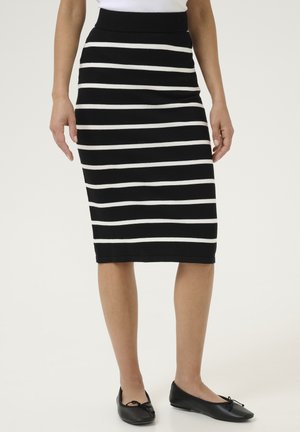 Jupe crayon en tricot avec des rayures horizontales noir et blanc, dotée d'une taille haute. Associée à des ballerines noires.