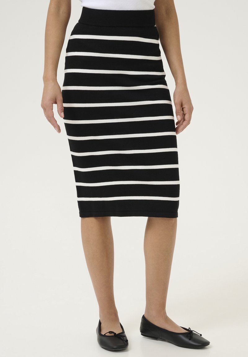 Jupe crayon en tricot avec des rayures horizontales noir et blanc, dotée d'une taille haute. Associée à des ballerines noires.