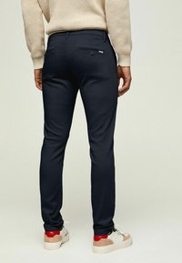 Marinblå byxor med slim fit, som har två bakfickor med dragkedja, slät yta och är matchade med avslappnade sneakers.