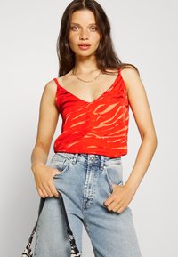 Top vermelho sem mangas com padrão de riscas de zebra, decote em V e finas alças nos ombros, combinado com jeans de cintura alta azul-claro.