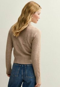 Maglione beige a maglia con orlo e polsini a coste, caratterizzato da un colletto classico e un design aderente. Abbinato a jeans blu a vita alta.