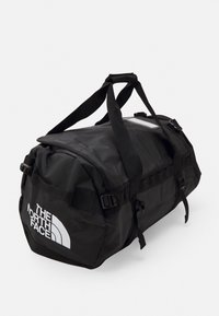 Sac de sport noir fabriqué en tissu durable, avec des poignées ajustables, des accents réfléchissants et un logo blanc bien visible à l'avant.
