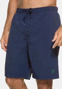Marineblaue Badeshorts aus leichtem Stoff, mit elastischem Bund und Kordelzug, Seitenentaschen und einem grünen Logoakzent.