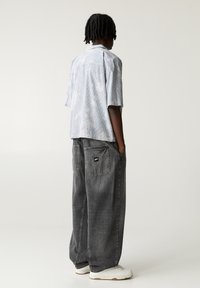Chemise à rayures bleu clair à manches courtes avec une coupe décontractée, associée à un pantalon en denim gris ample, doté de grandes poches et d'une étiquette de logo.