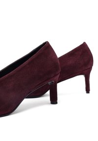 Zapatos de tacón alto de ante burdeos con punta afilada y un tacón delgado y texturizado. La superficie es lisa con un acabado mate.