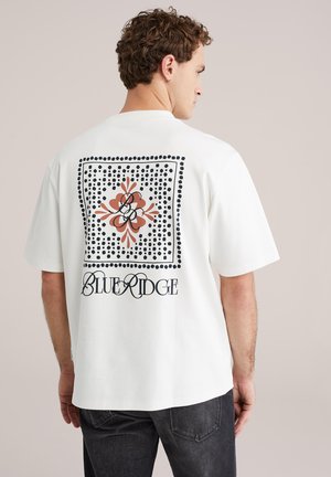 Wit T-shirt met een grote grafische print op de achterkant met een oranje bloemenontwerp, zwarte stippen en de tekst "BLUE RIDGE". Korte mouwen.