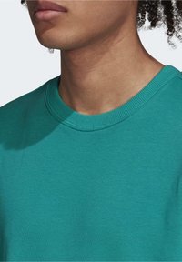 Turkos bomulls-T-shirt med rund halsringning. Kort ärm, texturerat tyg, slät halsringning och en avslappnad passform.