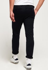 Pantaloni neri con una vestibilità su misura, dotati di due tasche posteriori e orli arrotolati. Indossati con sneakers bianche e calzini bianchi a coste.
