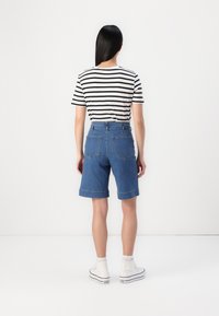 Calções de ganga com cintura alta, barras dobradas e dois bolsos traseiros, combinados com uma camisola de riscas pretas e brancas e ténis brancos.