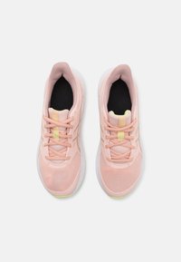 Des chaussures de sport rose clair avec un dessus en maille, un système de laçage, une semelle intérieure noire et un accent jaune sur la languette. Semelle extérieure en caoutchouc blanc.