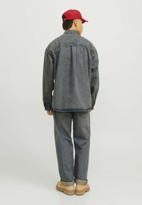 Giacca di jeans in una tonalità media con una vestibilità rilassata, caratterizzata da uno yoke posteriore e polsini con bottoni; abbinata a jeans grigi chiari e scarpe beige.