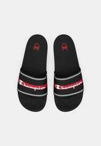Μαύρα σανδάλια με φαρδύ υφασμάτινο λουράκι που φέρει το λευκό και κόκκινο λογότυπο "Champion", με υφή στην επιφάνεια και στρογγυλεμένες άκρες.