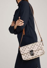 Crossbody bag in beige and grey checker pattern, featuring a front flap, silver hardware, and a brown leather strap. Textured finish.