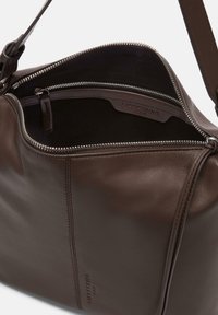 Brązowa skórzana torba na ramię z zamkiem błyskawicznym, charakteryzująca się gładką teksturą i tonową nicią. Wnętrze zawiera materiałowe wykończenie.