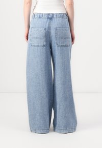 Lyseblå denim bukser med vid ben og linning, som har to bakre lommer og synlige sømdetaljer. Glatt tekstur, avslappet design.