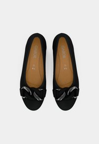 Svarte slip-on sko med glatt stoffoverdel, med en stor sølvkjede på forsiden og en brun polstret innersåle.