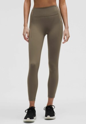 High-waisted olive green leggings made from a stretchy fabric, featuring a smooth texture and side seams for detailing, paired with black sneakers.
