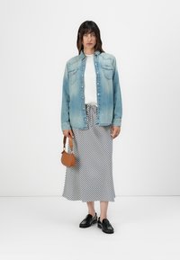 Lys blå denimskjorte, hvit topp, svart-hvitt stripete skjørt, svarte sko og liten brun håndveske. En enkel, uformell antrekksdesign.