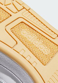 Adidasova potplat cipela s teksturiranim žutim gumenim gaznim slojem s uzorkom u obliku zigzaga i uzdignutim detaljima; iznad je srebrno-siva sintetička tkanina.