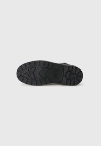 Suela de bota de goma negra con un patrón de relieve profundo, superficie texturizada y acentos elevados, diseñada para durabilidad y tracción.