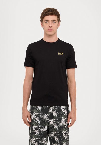 T-shirt noir à manches courtes en coton, avec un petit logo doré "EA7" sur la poitrine gauche. Design simple et ajusté, texture lisse.