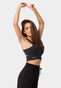 Melnā sportiskā apakšveļa ar asimetrisku griezumu un sānu izgriezumiem. Ir logotips apakšmalā un kopā ar melnajām sporta biksēm veido sportisku izskatu.