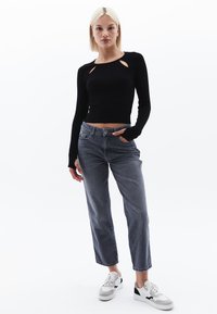 Maglietta a maniche lunghe nera a coste con ritagli a forma di chiave, abbinata a pantaloni in denim grigi a vita alta e sneaker bianche con accenti neri.