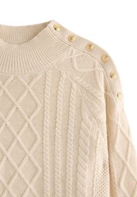 Cremefarvet strikket sweater med strukturerede kabelmønstre, ribbet halsudskæring og seks guldknap detaljer på venstre skulder.