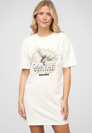 Weißes Baumwoll-T-Shirt-Kleid mit einem grafischen Design, das einen Adler zeigt, sowie den Aufschriften "CANYON WANDERER" und "WILD CHILD" in schwarzer und goldener Schrift.