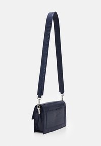 Granatowa torba na ramię z ekoskóry o fakturze imitującej skórę krokodyla, z płaską przednią kieszenią oraz długim, regulowanym paskiem ze srebrnymi okuciami.