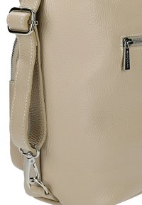 Beige leren tas met een textuurafwerking, voorzien van een zilveren rits en beslag. De schouderband is verstelbaar en heeft een sluitingdetail.