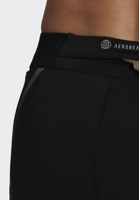 Pantaloni sportivi neri con vita a coste, cuciture piatte e un piccolo logo in evidenza. Il materiale sembra liscio ed elasticizzato.