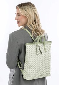 Sac à dos vert clair avec un motif géométrique texturé, deux poignées supérieures, des bretelles ajustables et une fermeture zippée avec une petite étiquette décorative.