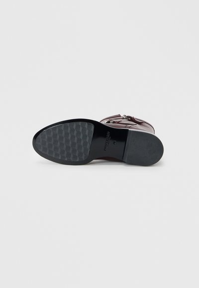 Black rubber outsole with a textured hexagonal pattern; burgundy leather upper with buckle hardware and ankle strap detailing.