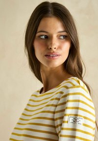 Gestreiftes Langarmhemd aus weißer und gelber Baumwolle. Verfügt über einen runden Halsschnitt und ein Label-Patch am linken Ärmel. Glatte Textur.