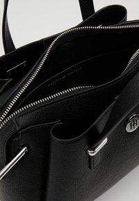 Musta nahkalaukku, jossa on teksturoitu pinta, hopeiset yksityiskohdat, vetoketjukiinnitys ja useita osastoja. Brändin logo näkyy sisällä.