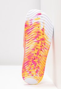 Semelle de chaussure avec motif ondulé en blanc, orange et rose, présentant des perforations circulaires alignées verticalement sur la semelle.