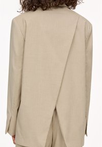 Beige pinstriped blazer with a split back, tailored design,structured shoulders, and side vents; textured fabric.