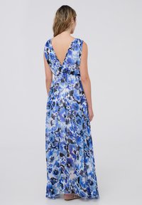 Abito lungo con stampa floreale in diverse sfumature di blu, design con profondo scollo V sul retro, senza maniche e in tessuto leggero e trasparente.