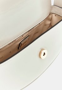 Borsa a mano in pelle bianca lucida con una texture liscia, chiusura in ottone dorato e interno beige con il logo del marchio in un motivo.