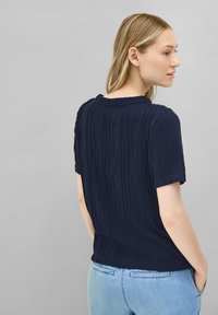 Top de manga corta en color navy con rayas verticales texturizadas, presenta un escote redondo y un corte relajado, combinado con jeans de color azul claro.