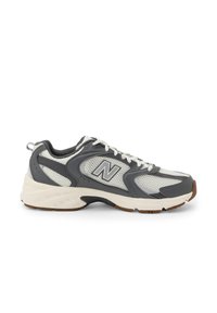Šedé a bílé atletické tenisky New Balance s síťovinovými panely, polstrovaným límcem, bílými tkaničkami a béžovou podešví s černými a hnědými vzorovanými akcenty.