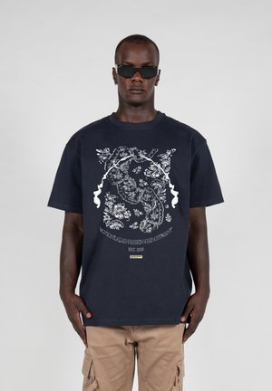 Marineblå bomulds t-shirt med hvidt blomstermotiv og tekst. Korte ærmer, rund hals, afslappet pasform. Bæres med beige cargo-bukser.