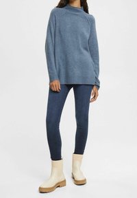 Ljusblå stickad tröja med hög hals, tillsammans med mörkblå figurnära jeans och krämfärgade ankelstövlar med en robust sula.