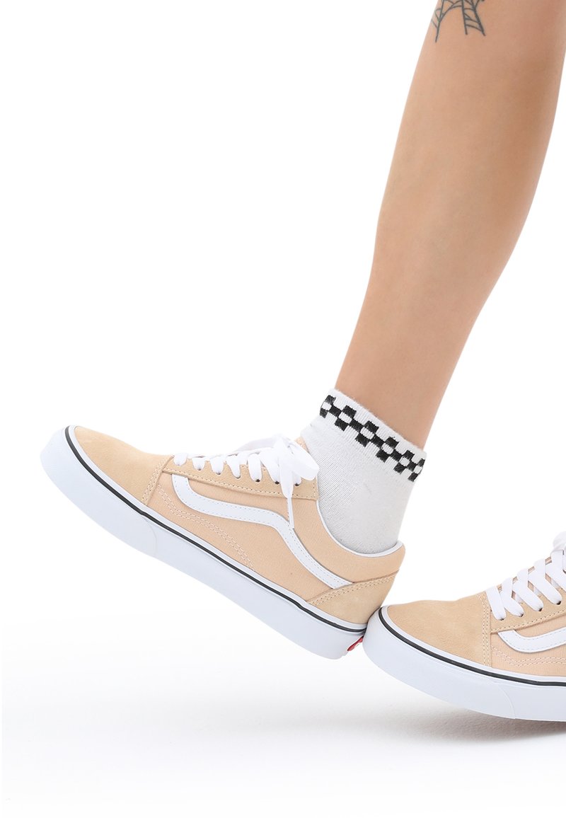 Beige mokkasiner av semsket skinn med hvite detaljer og snøring. Svart-hvite rutete ankelstrømper synlige. Lavt design med gummisåler.